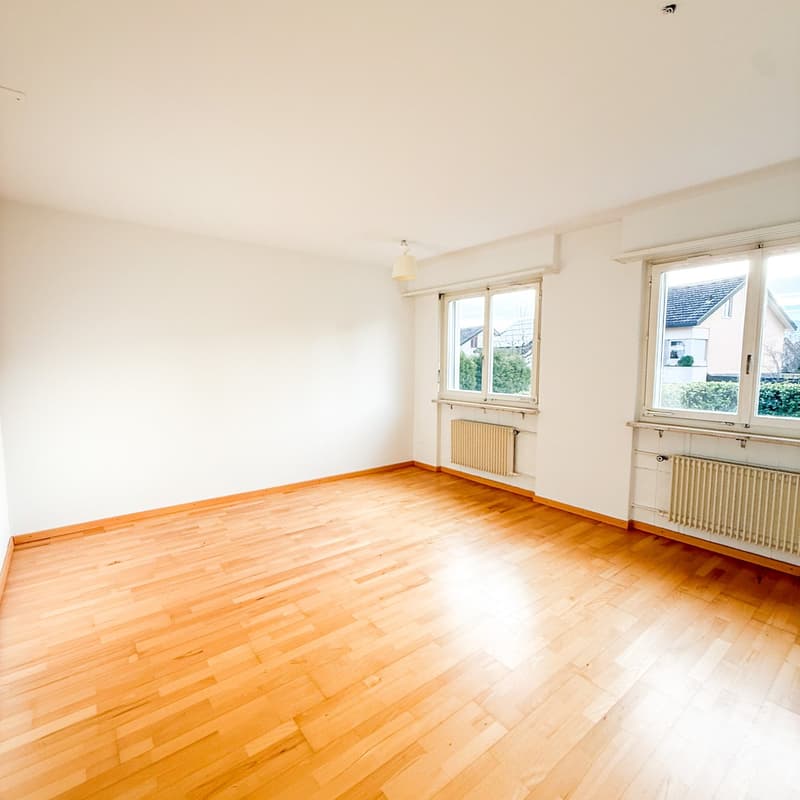 Empty room with wooden floors, white walls, two windows, white radiators.