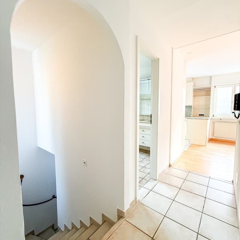 corridor with tiled floor, white walls, arch shaped wall at left, staircase, open door on right