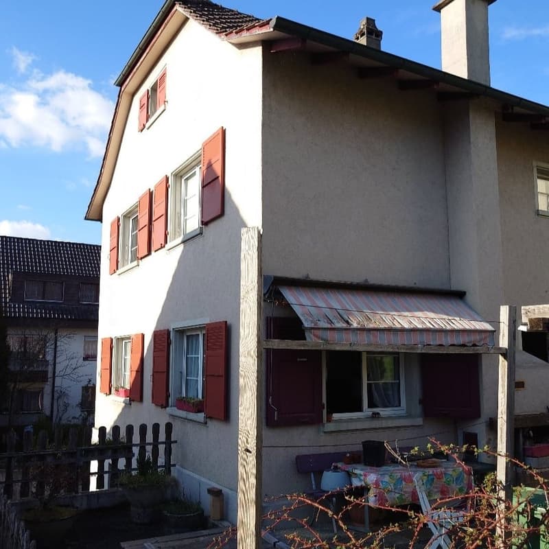 Three story house, brick facade, red shutters, awning, fence, small garden with tables and chairs
