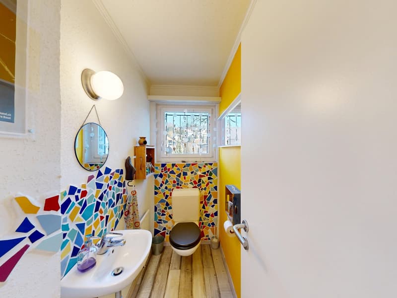 small bathroom with white sink, colorful mosaic tiles, toilet, mirror, window, wooden floor