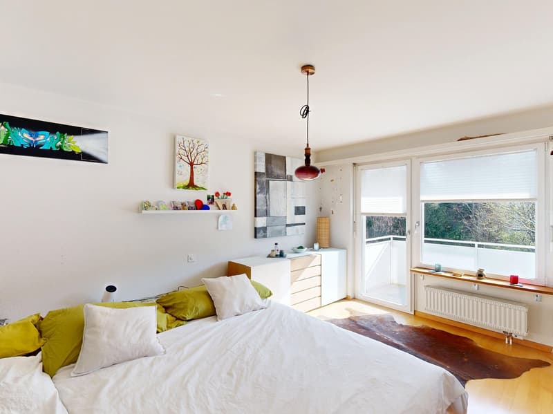 large bed, white sheets, white and yellow pillows, white walls, white ceiling, white radiator, white cabinet, white shelves, white and green artwork, balcony, sliding glass door, white blinds, wooden floor