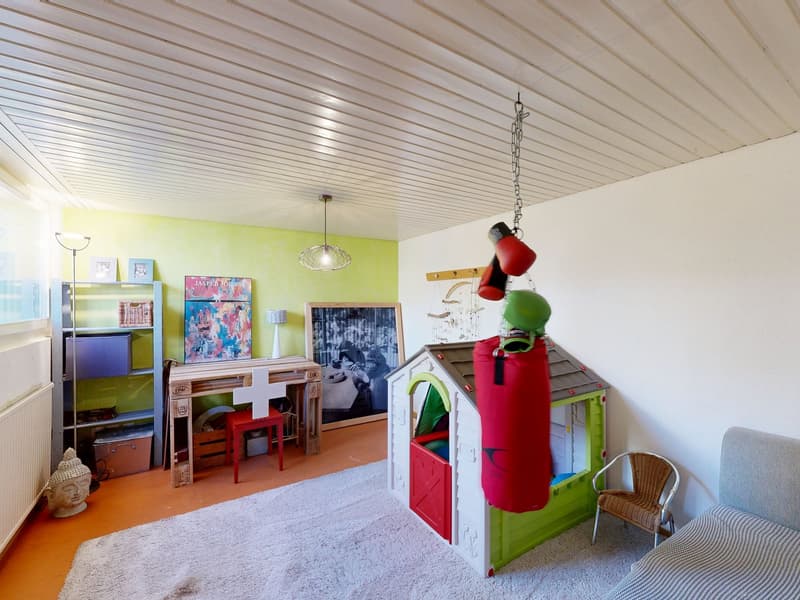 A room with a white ceiling, green and white walls, a white rug, a desk, a chair, a punching bag, a shelf, a picture frame, a lamp, a Buddha statue, and a white radiator.