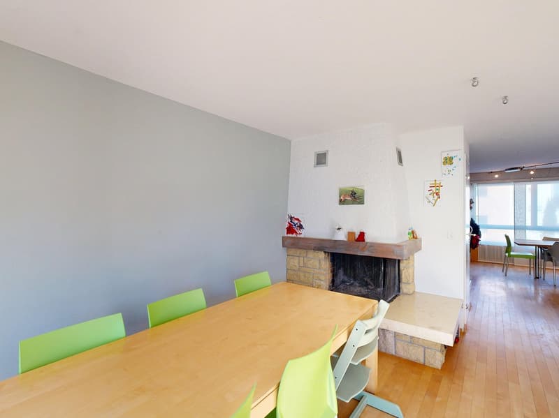 Dining room with a fireplace, wooden table, green chairs, wooden floor, gray walls