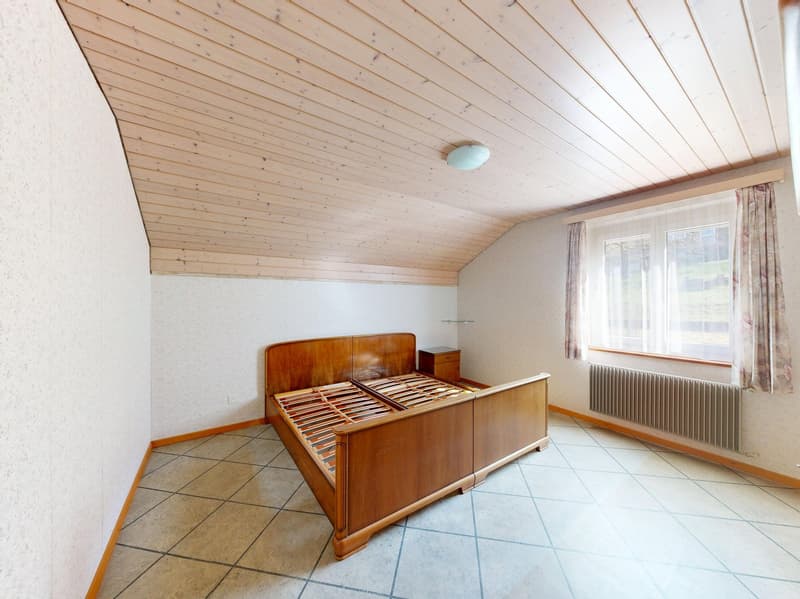 Empty room with wooden bed, wooden ceiling, tiled floor, white walls, window with curtains, radiator