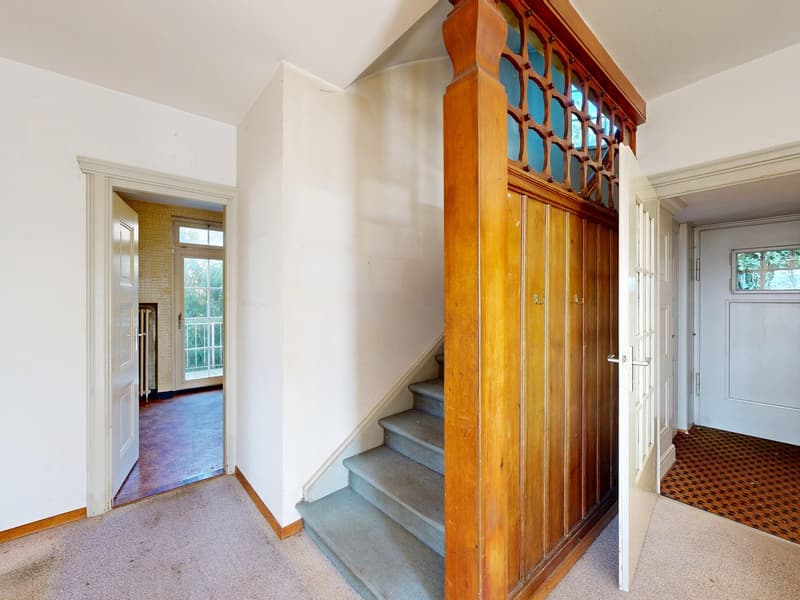 Entrance hall with wooden staircase, white walls, carpeted floor, open doors leading to rooms
