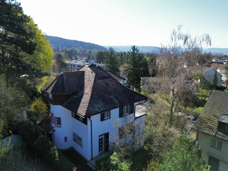 2 story house, white exterior, brown roof, surrounded by trees, balcony on the second floor