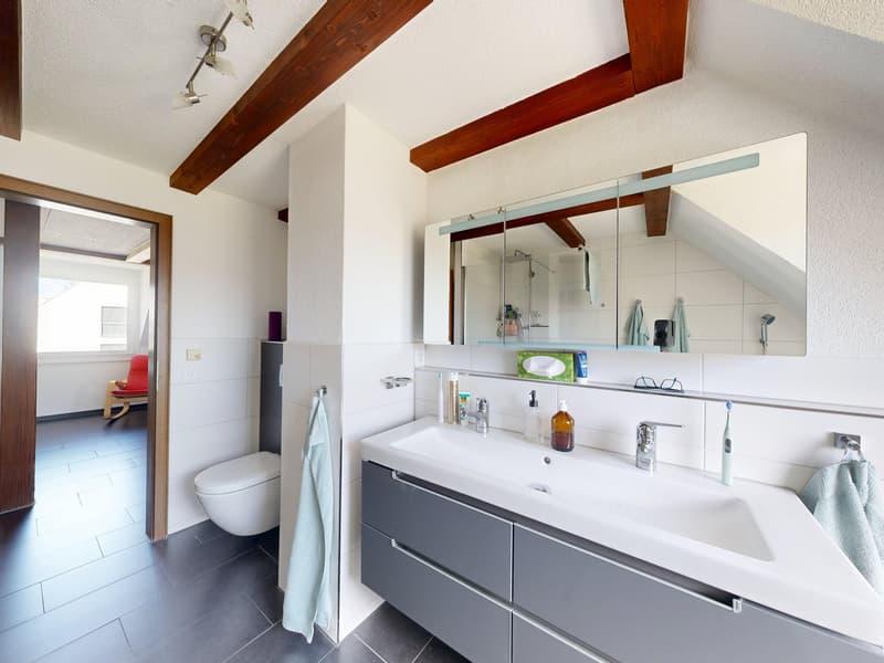 modern bathroom with white tiles, wooden beams, white sink, mirror, toilet, and a shower