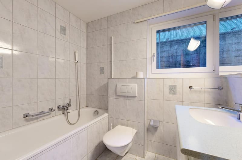 Bathroom with white tiles, bathtub, toilet, sink, and window