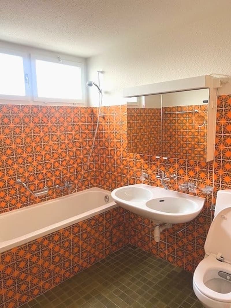 Bathroom with orange tiles, bathtub, double sink, toilet, and a shower head attached to the wall.