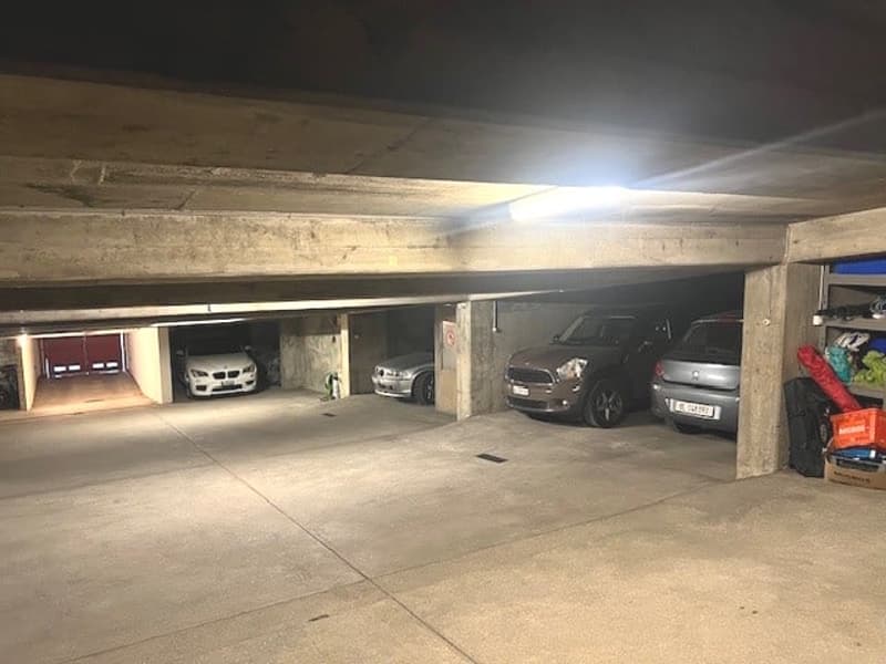 underground parking with concrete walls, several vehicles, visible lighting