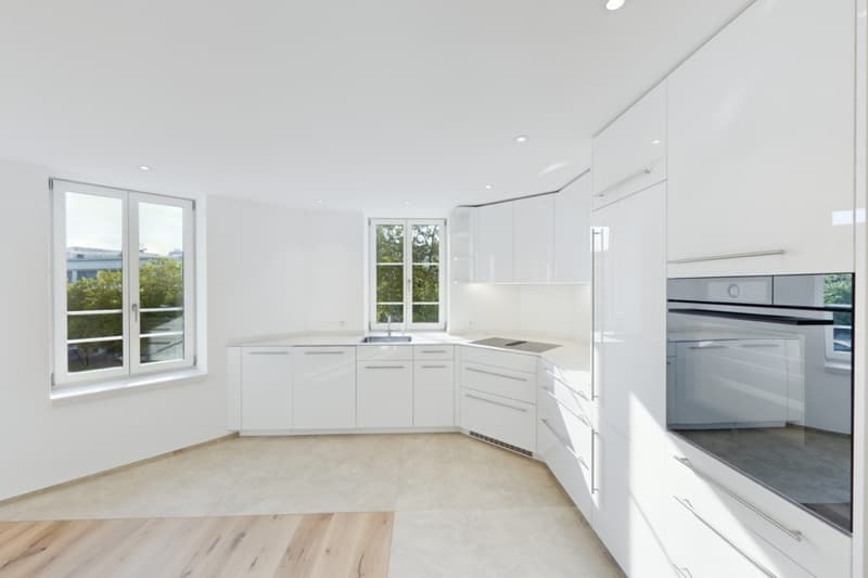 Spacious, modern kitchen with white cabinets, stainless steel appliances including a dishwasher, and large windows providing natural light