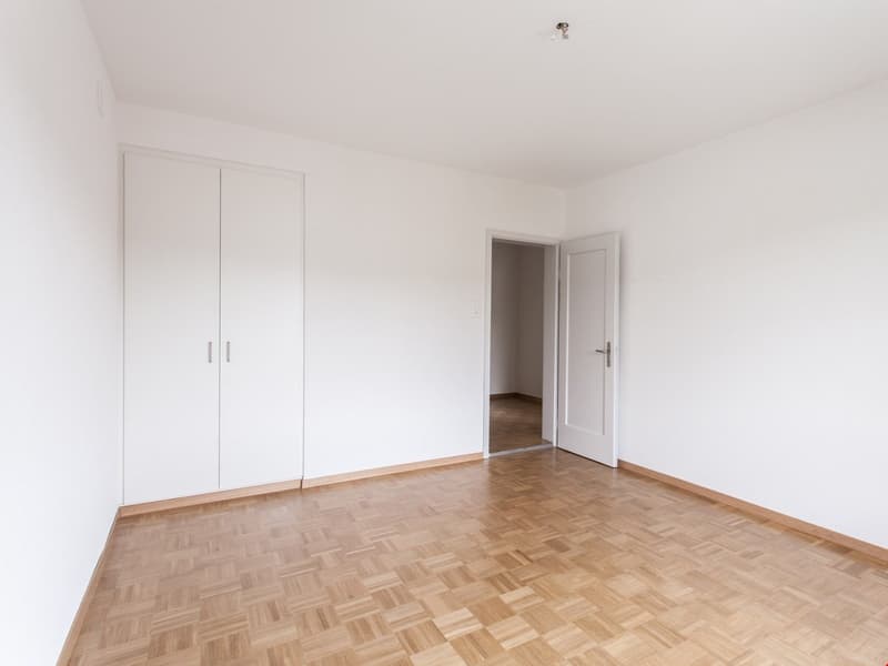 Empty room, white walls, wooden parquet floor, white cabinets, doorway