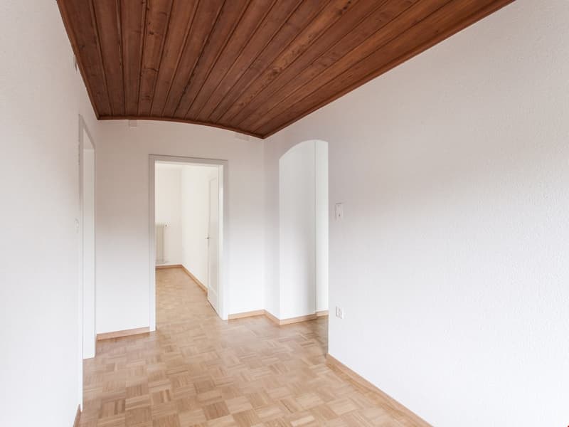 Empty room, wooden parquet flooring, wooden ceiling, two white walls, arched doorway