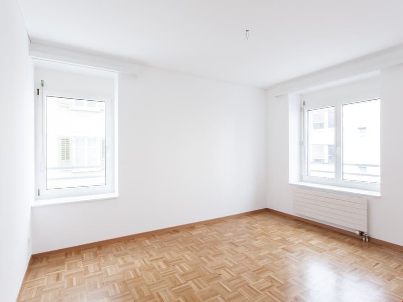 empty room, white walls, wooden floor, two windows, radiator