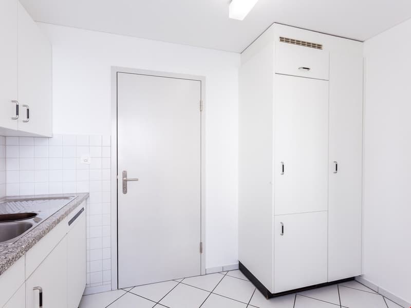 modern kitchen with white cabinets, white tiled floor, white walls, double sink, white door, white wardrobe