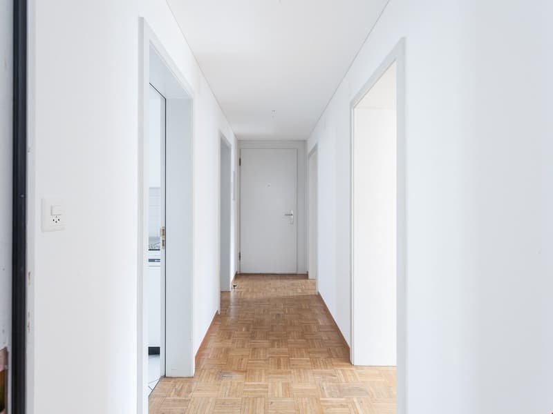 Empty hallway with white walls, wooden floor, and doors on both sides