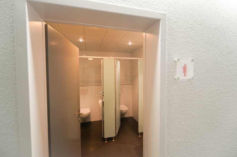 The image shows a bathroom with two toilet stalls and a private washing machine visible.