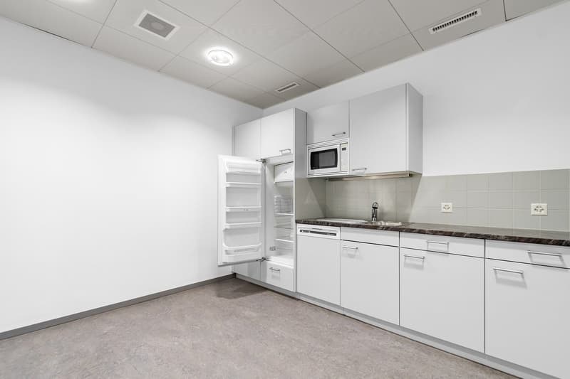 Modern, white kitchen with built-in appliances including a refrigerator and microwave, granite countertops, and tile backsplash.