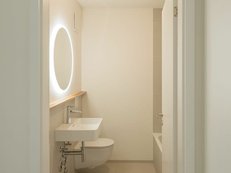 Badezimmer mit Badewanne, WC, Lavabo und modernem Rundspiegel