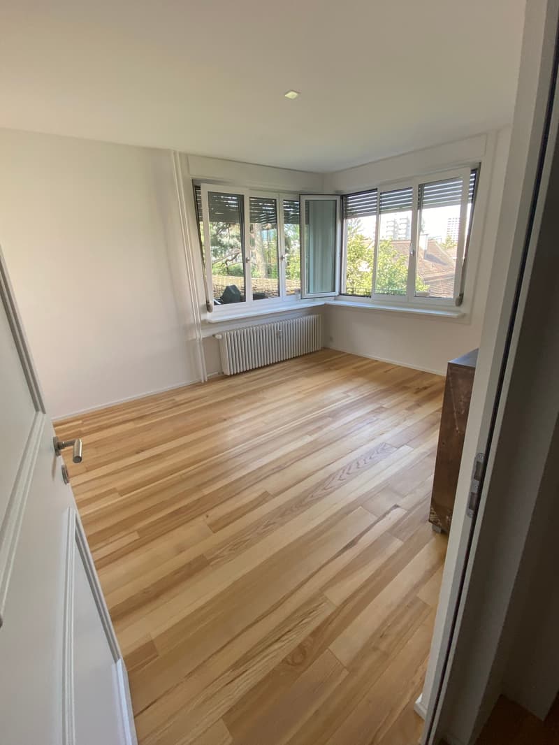 Spacious bedroom with hardwood flooring, large windows providing natural light, and a balcony or terrace visible.