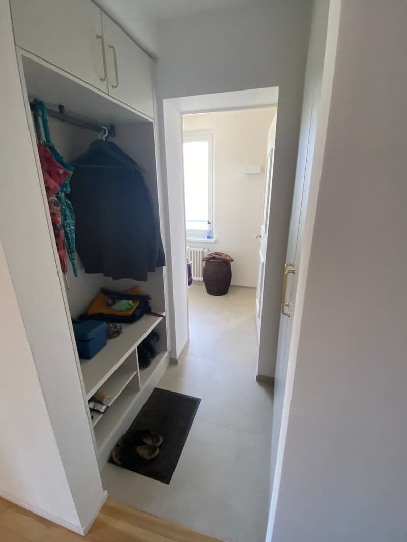 The image shows a bedroom with a built-in wardrobe, a doorway leading to another room, and a rug on the floor.
