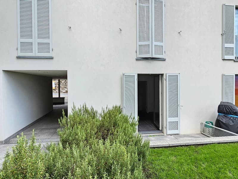 White building with white shutters, open door, paved walk, green bush, white wall