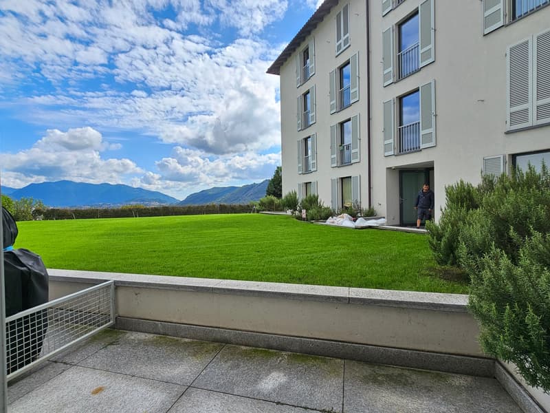 Building exterior, balcony with plants, green lawn, mountains in the background