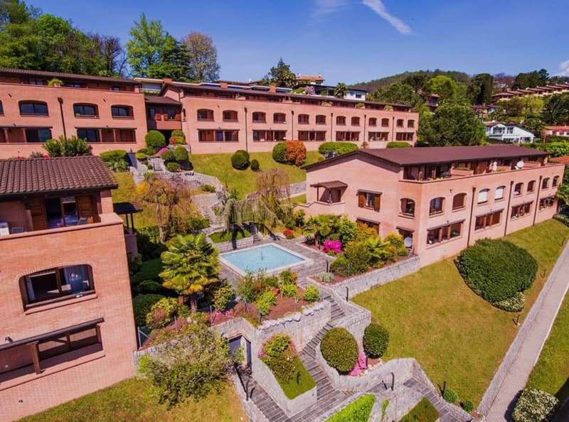 Several buildings on sloped terrain, swimming pool in center, green surroundings, staircases connecting levels