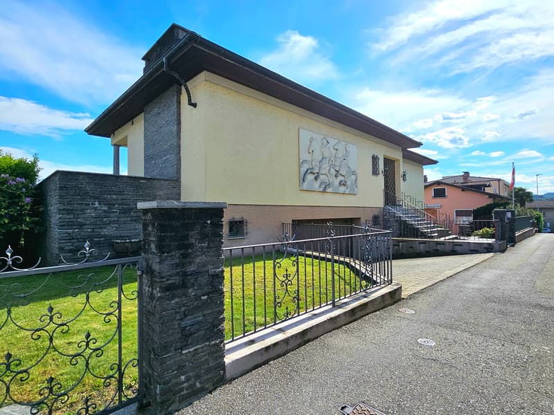 2 story house, yellow walls, brick wall, black railings, staircase, driveway, gate, grassy lawn, clear blue sky