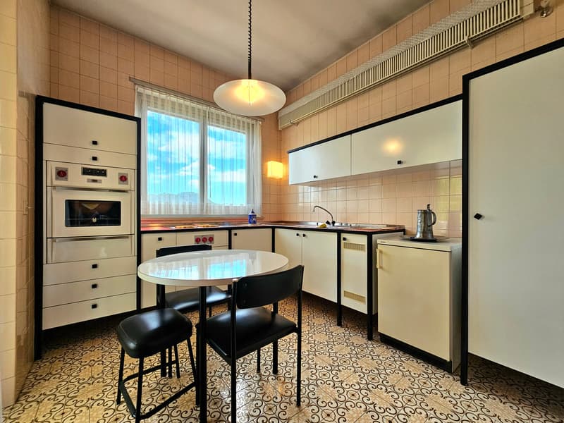 modern kitchen, white tiled walls, white cabinets, stainless steel appliances, pendant light, round table with black chairs, window with white curtains