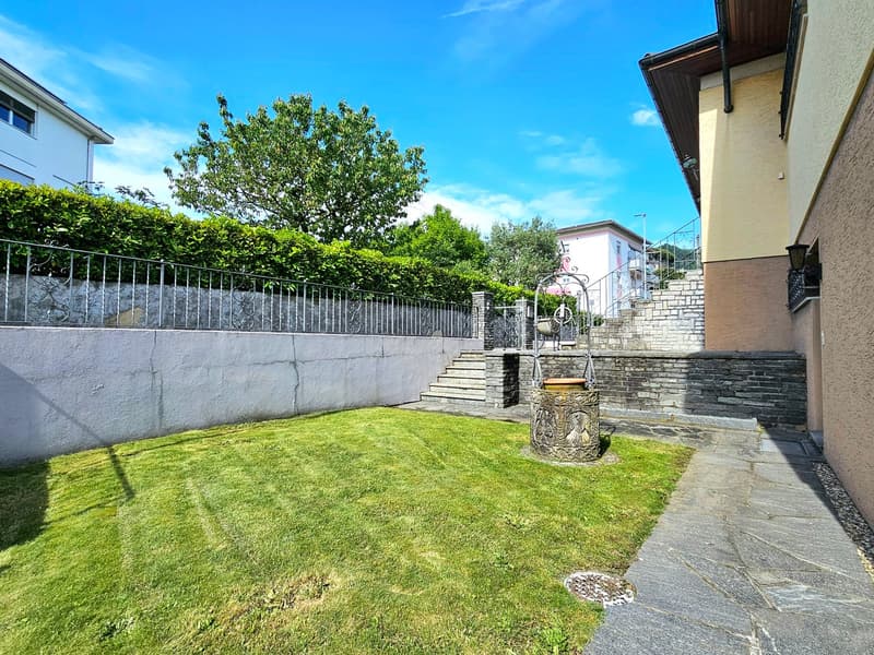 Green lawn, gravel pathway, decorative well, wall fence
