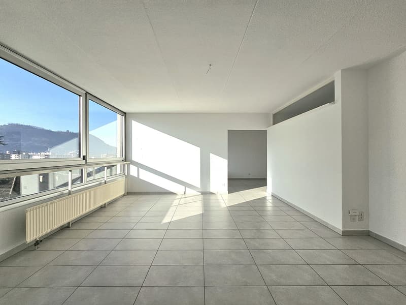 Empty room with large windows, tiled floor, white walls, visible mountains in the distance