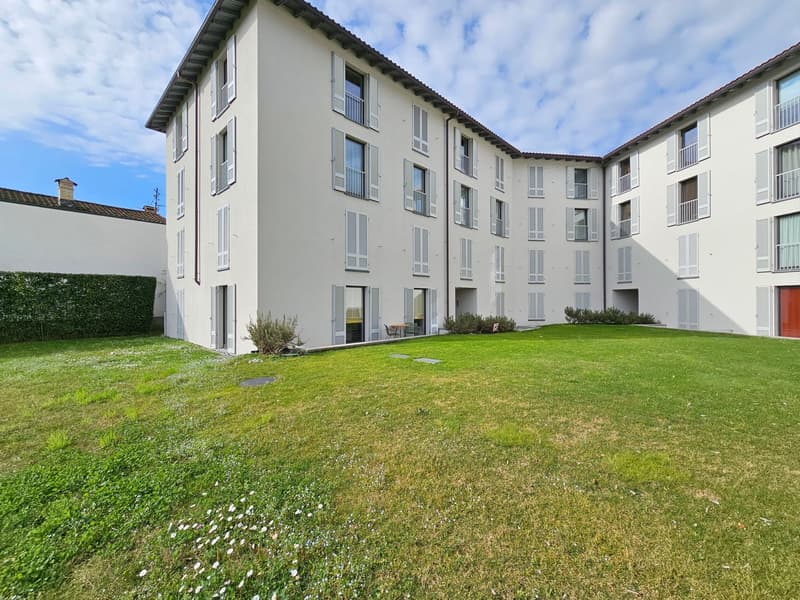 modern apartment building, white walls, many windows, large lawn, green bushes