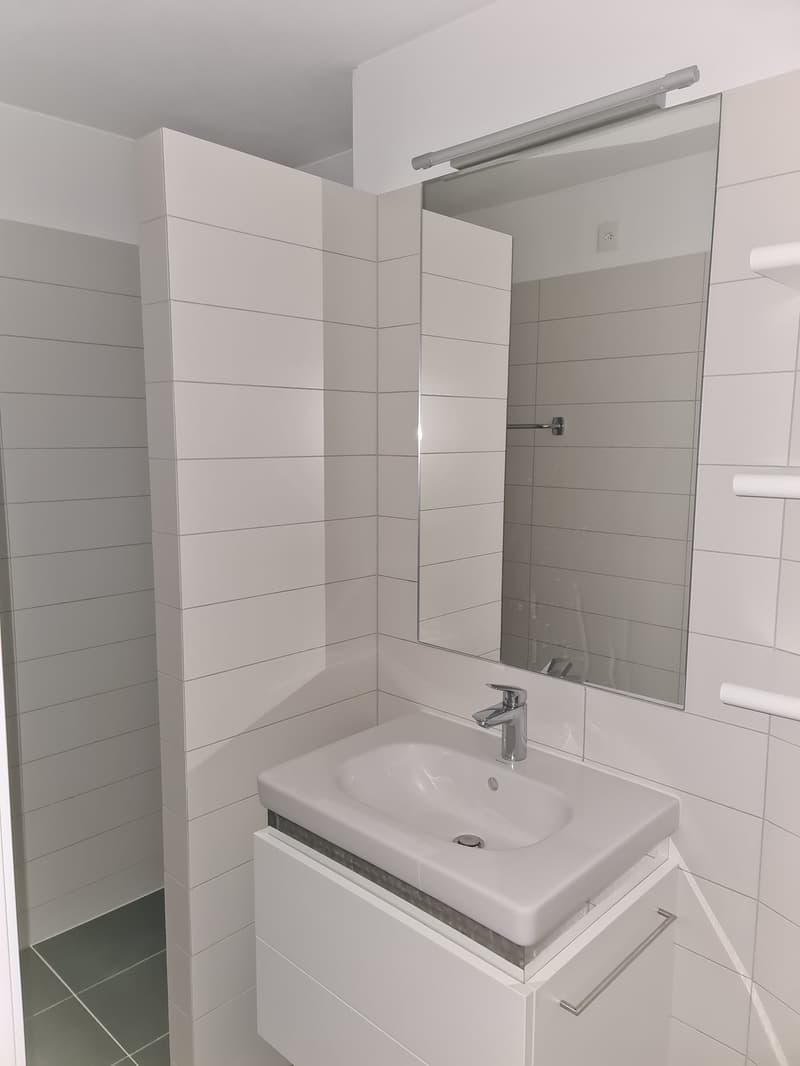 modern bathroom with white tiles, white sink, silver faucet, full mirror, white cabinet with sink, white wall