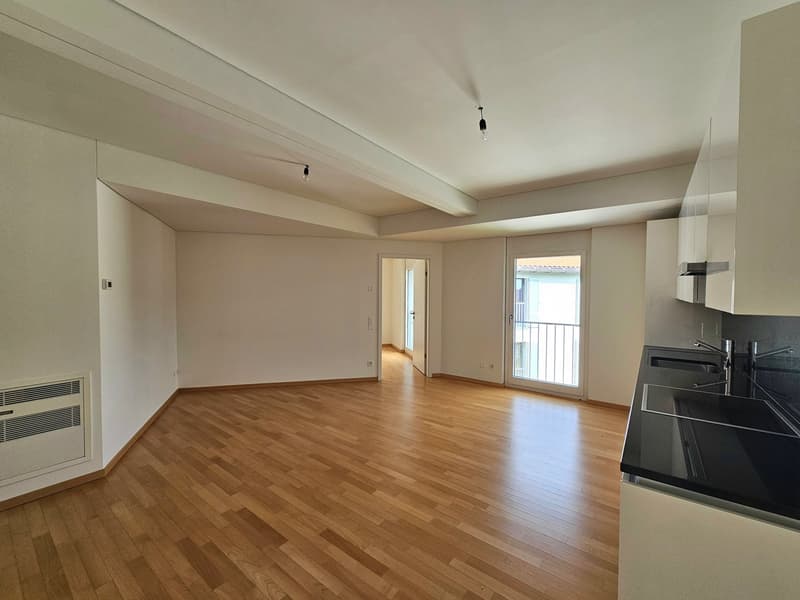 empty room, hardwood floors, open kitchen, sliding glass door leading to balcony, recessed lighting