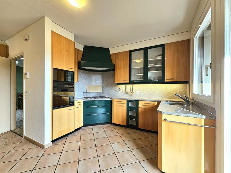 Modern kitchen with wooden cabinets, tiled floor, gas stove, microwave, dishwasher, sink, and a separate washing machine area.