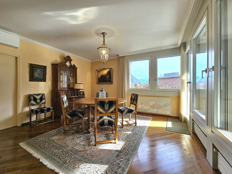 Dining room: wooden floor, large windows, wooden table and chairs, chandelier, rug, cabinet, artwork, radiators