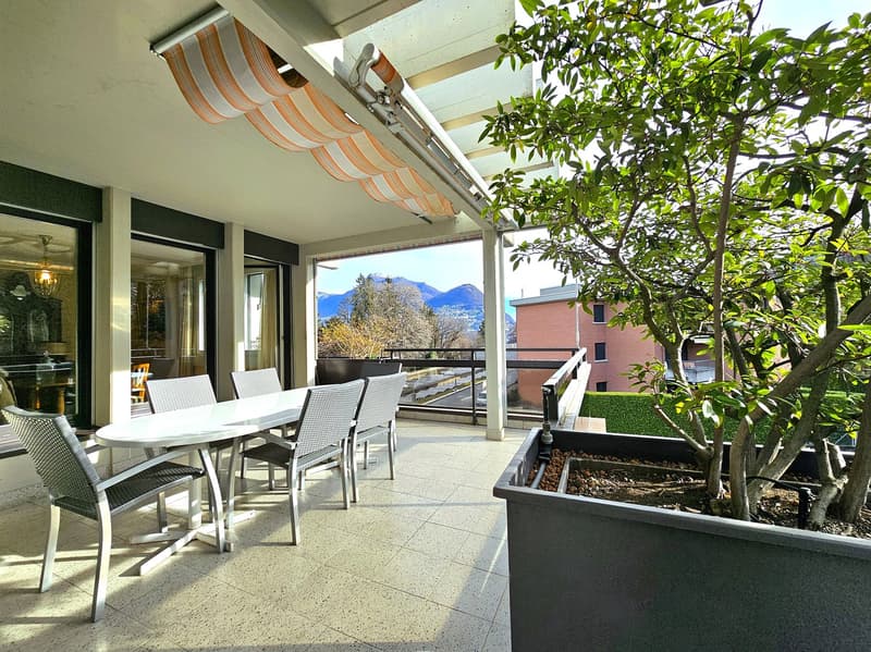 covered terrace, round dining table, cushioned chairs, glass doors, balcony railing, tree, open view of mountains