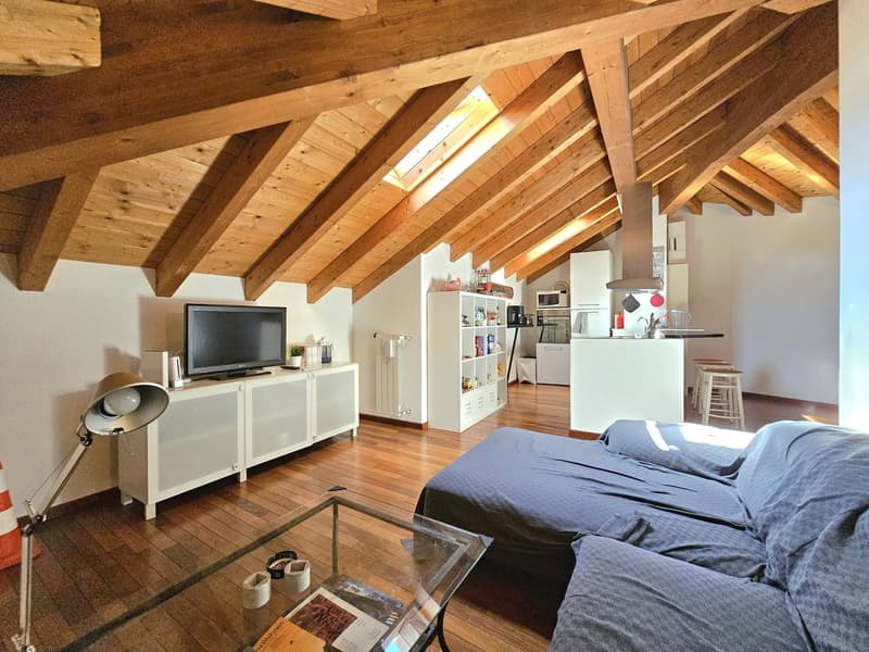 open living room with kitchen, wooden ceiling beams, wooden floors, sofa, table, lamp, tv stand with flat screen tv, coffee table, kitchen island, microwave, fridge, stove, stools, desk with books