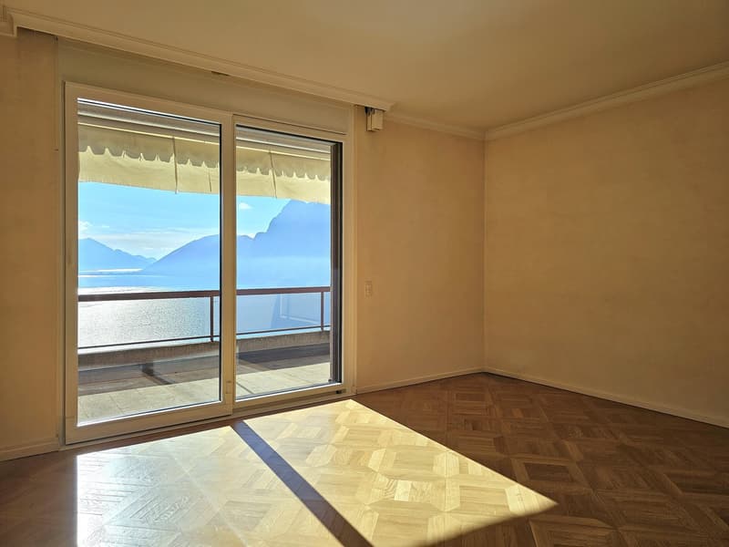 sliding glass door leading to balcony, wooden parquet floor, white walls, bright sunlight, ocean view, mountains in the distance
