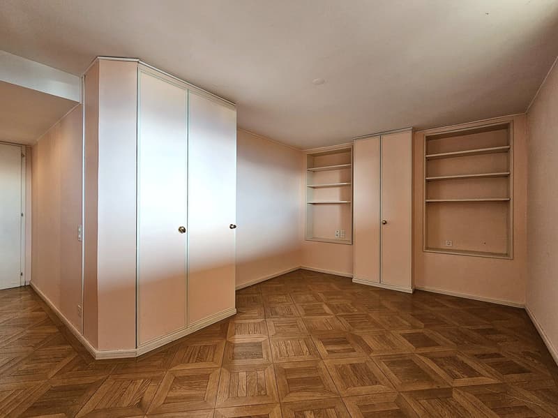 wooden parquet flooring, two large built-in wardrobes, shelves on the wall, door on the left side, power outlets on the wall