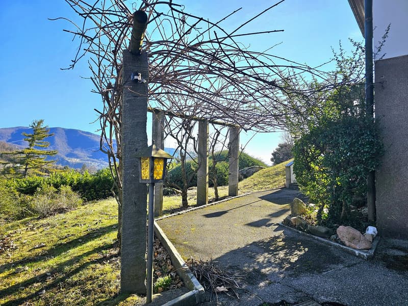 covered walkway, trellis with dried plants, lamps, grassy hill, distant mountains