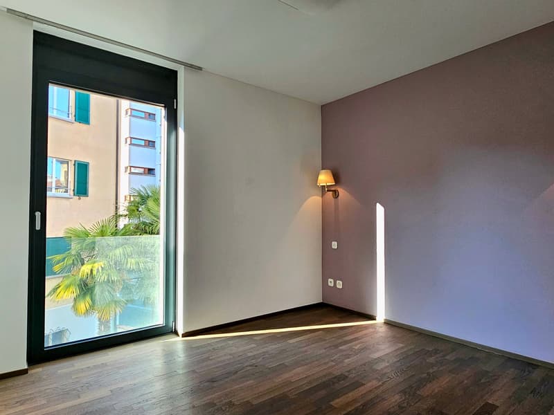 empty room, large glass door, wooden floor, white and purple walls, wall lamp, view of a palm tree