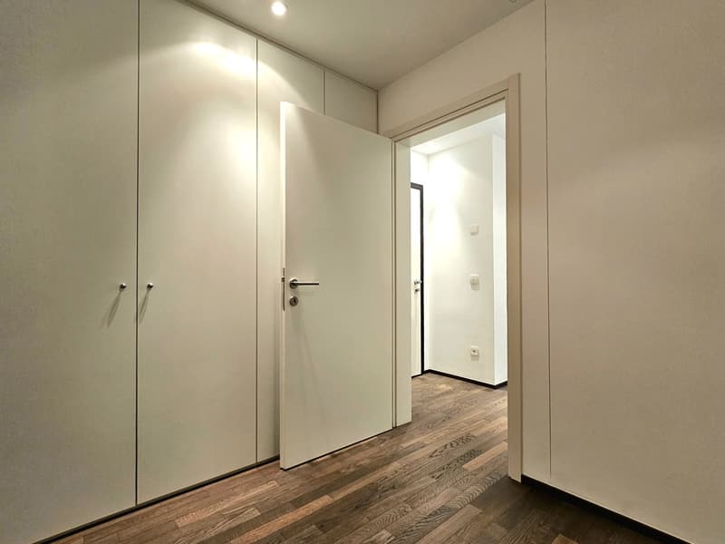 Empty room with white walls, wooden floor, two closets, open door, and another room visible