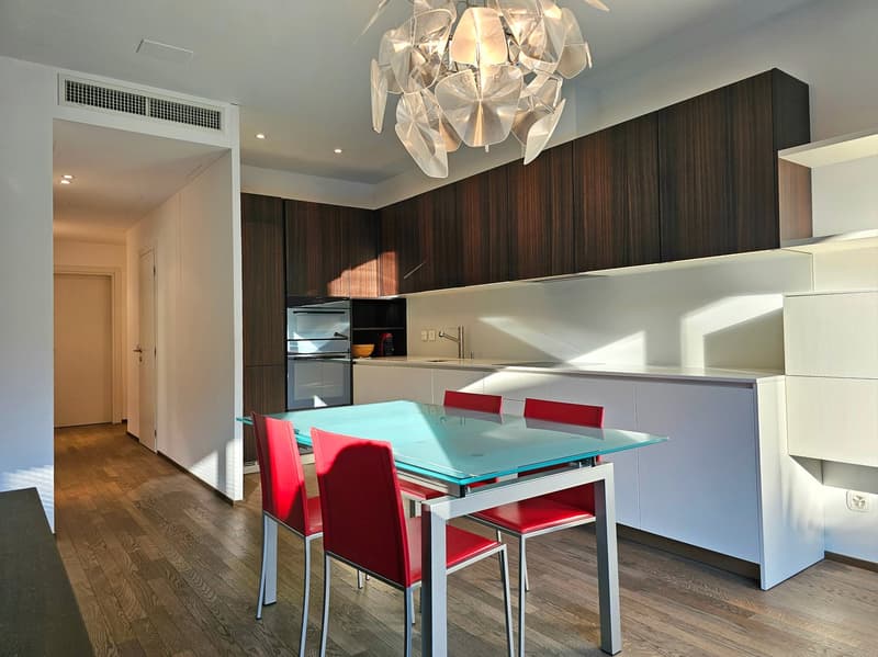 modern kitchen with glass table, red chairs, wooden floor, white cabinets, chandelier, sink, oven