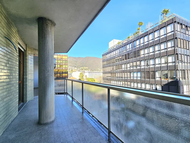 Balcony with glass railing, tiled floor, pillar, view of a building and mountain