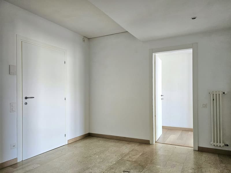 Empty room with white walls, wooden floor, two doors, and a radiator on the right wall.