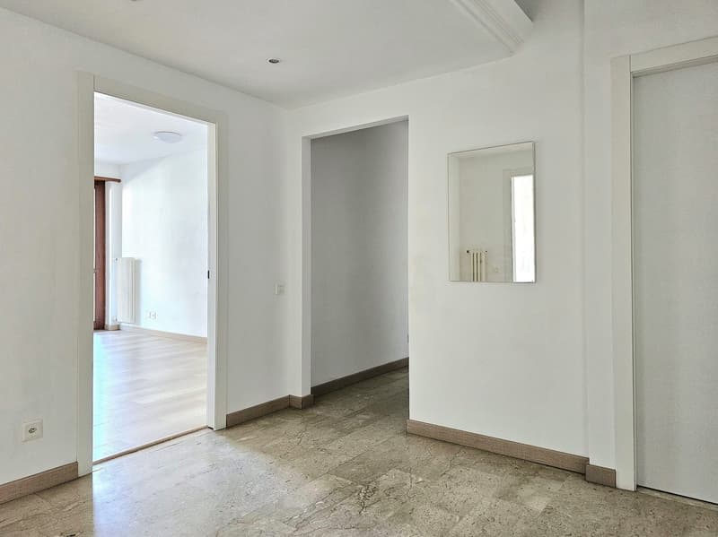 Empty room with white walls, wooden floor, mirror on the wall, open door leading to another room