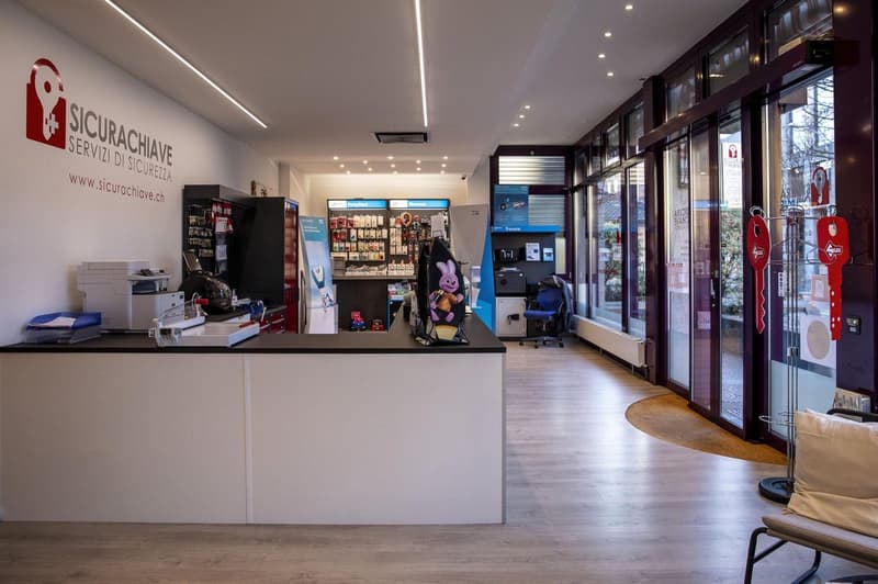 Reception desk, printer, shelves with products, glass doors, glass windows, wooden floor, radiator, chair, cushion