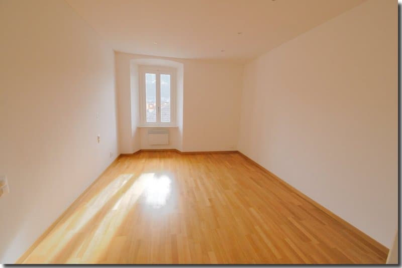 empty room with hardwood floor, white walls, large window, power outlets, window sill
